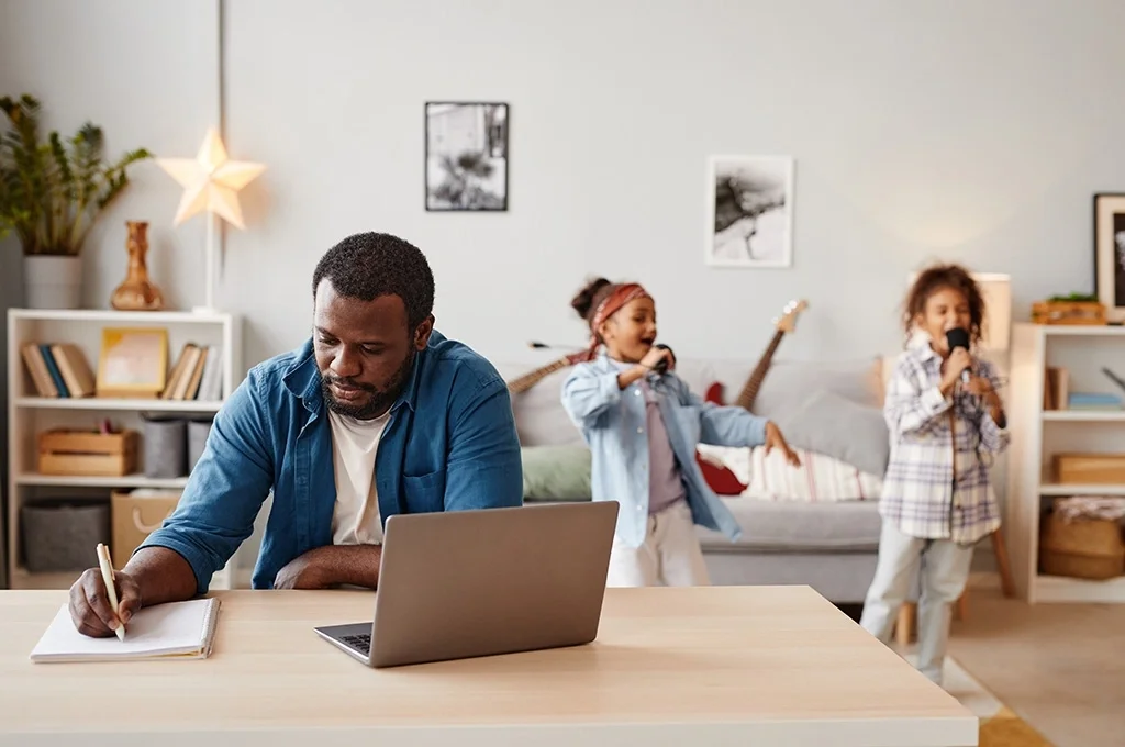 A veteran comparing savings account requirements at home while his daughters play in the background