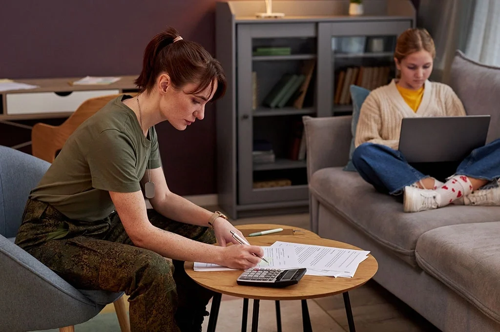 A veteran and her daughter sit in their living room while the veteran examines her finances