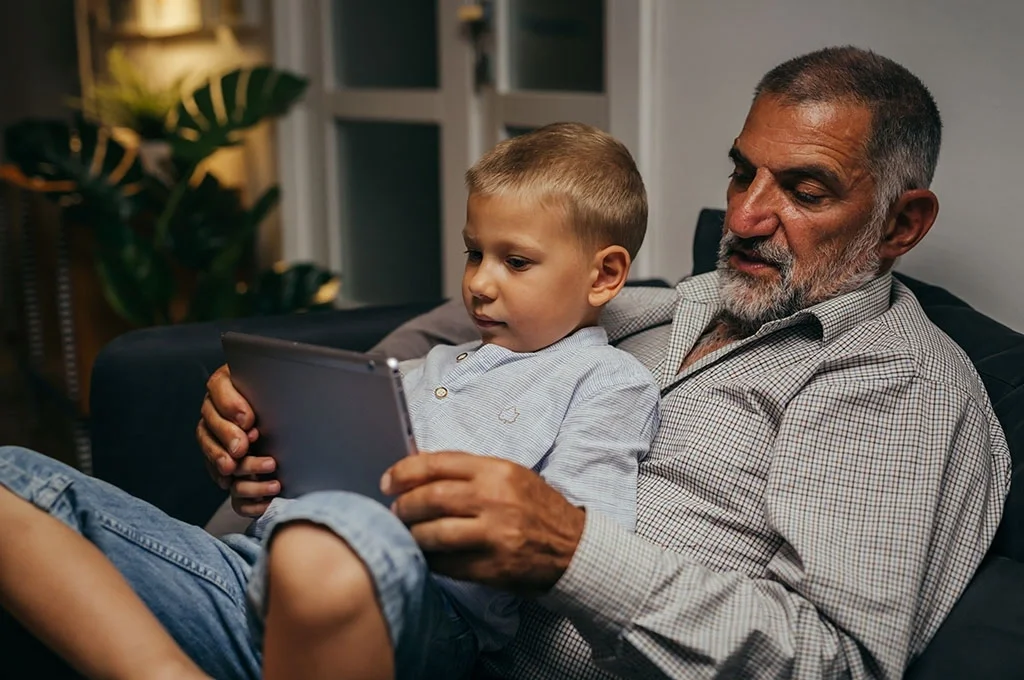 A grandfather spends time on the tablet with his grandson